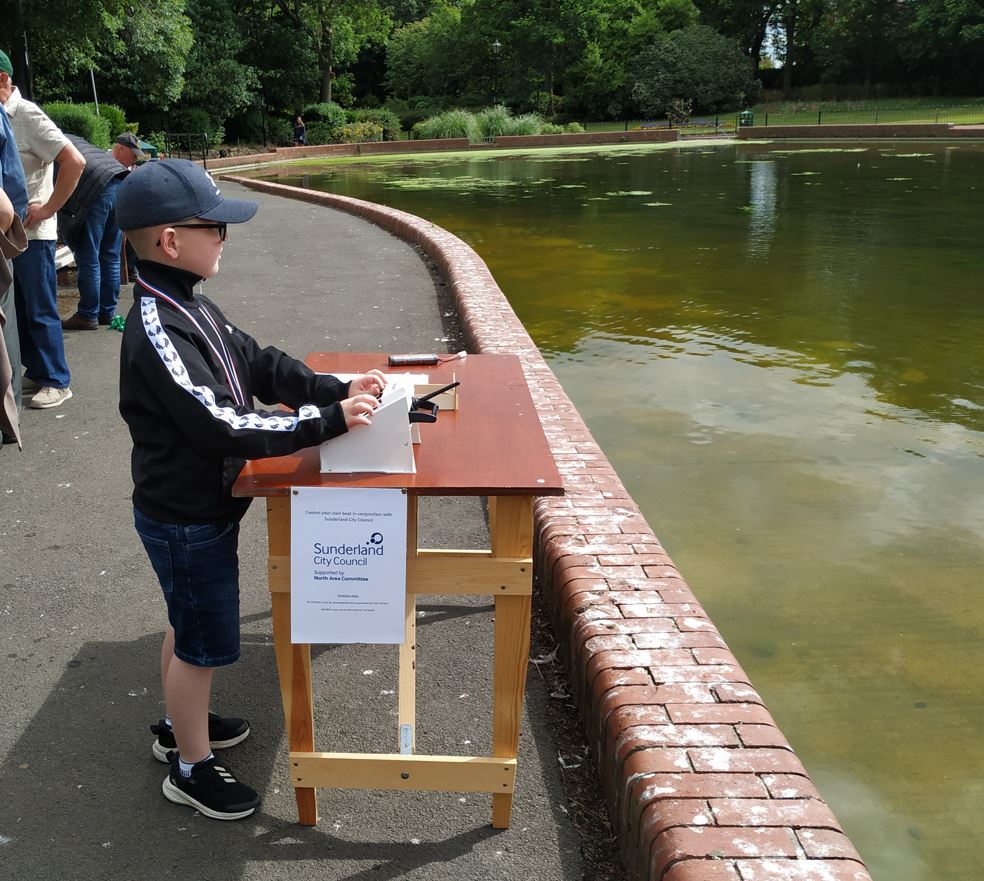 picture of a table beside the boating lake with one of the constructed model boats in use by a small boy.